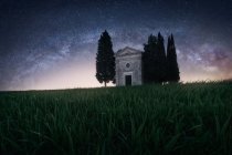 Beautiful peaceful landscape of small chapel with trees in remote empty green field against starry sky, Italy — Stock Photo