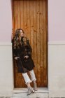 Стильная женщина в винтажном кожаном пальто, стоящая возле деревянной двери на улице — стоковое фото