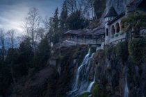 Каскад воды, падающий со скалистой скалы со зданием выше, Швейцария — стоковое фото