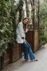 Stilvolle junge Frau sitzt auf Pflanzkübel im Garten und lacht — Stockfoto