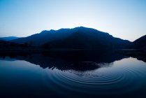 Pittoresca vista della superficie dell'acqua vicino a incredibili colline rocciose al tramonto e cielo blu — Foto stock