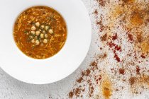 Traditionelle Harira-Suppe für Ramadan im Teller auf weißer Tischplatte mit verstreuten Gewürzen — Stockfoto