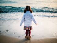 Anonymes kleines Mädchen von hinten, das am Strand auf Sand steht und auf das Meer blickt — Stockfoto