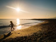 Silhouette eines nicht wiederzuerkennenden Mädchens, das bei Sonnenuntergang an der Küste spaziert — Stockfoto