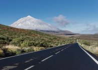 Asphalt countryside road through grassy terrain near magnificent snowy mountain peak on sunny day on Canary Islands, Spain — Stock Photo
