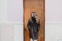 Stylish woman in vintage leather coat standing near wooden door on street — Stock Photo