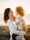 Женщина средних лет с дочерью на берегу моря улыбаются и обнимают друг друга — стоковое фото