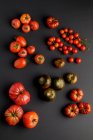 Verschiedene frische reife Tomaten auf schwarzer Oberfläche verstreut — Stockfoto