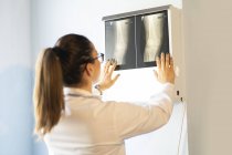 Молода жінка-лікар в уніформі дивиться на рентгенівське зображення на стіні в кімнаті — стокове фото