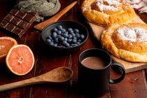 Pomme rouge fraîche et bleuets mûrs placés sur une table de bois près d'une tasse de boisson chaude aromatique et un délicieux pain pour le petit déjeuner le matin — Photo de stock