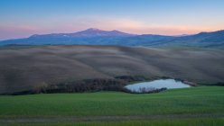 Paesaggio maestoso di verde valle con campi, lago e catena montuosa al tramonto in Toscana — Foto stock