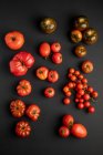 Tomates mûres fraîches et variées éparpillées sur la surface noire — Photo de stock