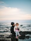 Niedliche Szene, wie Papa ihre kleine Tochter im Winter am Strand hält und umarmt — Stockfoto