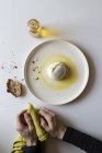 Mani di anonimo che tengono il tovagliolo verde vicino al piatto con gustosa burrata e pezzo di pane con olio su sfondo bianco — Foto stock