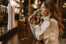 Стильна жінка п'є вино за стійкою в барі — стокове фото