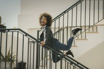 Excited African American female looking at camera and screaming while leaning on railings and jumping on building stairs — Stock Photo
