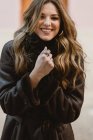 Стильная улыбающаяся молодая женщина в винтажном кожаном пальто смотрит в камеру — стоковое фото