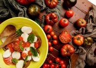 Fresh ripe tomatoes on wooden tabletop near bowl of yummy Caprese salad — Stock Photo