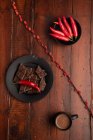 Tazza di bevanda calda fresca posta sul piano del tavolo del legname vicino al piatto con pezzi di cioccolato e peperoncino — Foto stock