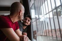 Romantic gay couple standing at window together — Stock Photo