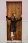 Усміхнена стильна жінка в старовинному шкіряному пальто, що стоїть біля дерев'яних дверей на вулиці — стокове фото