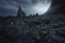 Живописный вид каменистого берега с острым скалом на фоне мрачного облачного неба — стоковое фото
