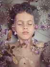 De cima a cara da criança no líquido entre pétalas frescas de flores — Fotografia de Stock