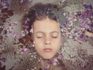 Du dessus de la face de l'enfant dans un liquide entre les pétales frais de fleurs — Photo de stock