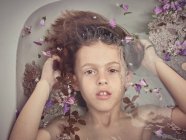 De cima a cara da criança no líquido entre pétalas frescas de flores — Fotografia de Stock