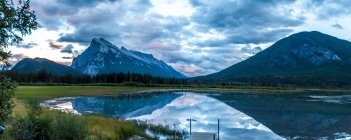 Pittoresca vista della superficie dell'acqua e della riva con colline di pietra e cielo nuvoloso a Banff, Canada — Foto stock