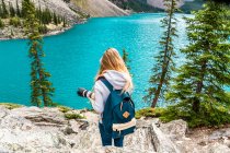 Vista posteriore del turista con zaino ripresa sulla macchina fotografica pittoresca vista della superficie dell'acqua e colline di pietra e cielo nuvoloso a Banff, Canada — Foto stock