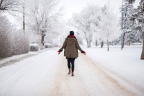 Visão traseira da mulher no desgaste do inverno indo na estrada no parque nevado em Banff, Canadá — Fotografia de Stock