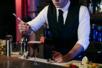 Молодой элегантный бармен, работающий за барной стойкой, готовит напиток в стакане — стоковое фото