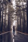 Traveler taking photo while walking on empty road in woods — Stock Photo