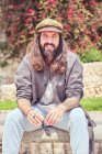 Стильний бородатий чоловік з довгим волоссям сидить у парку — стокове фото