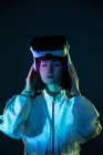 Jeune femme avec des lunettes de réalité virtuelle regardant loin dans la lumière au néon — Photo de stock