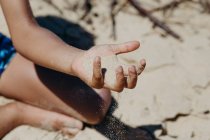 Adorable African American boy in casual outfit playing with dry sand while spending time in yard on sunny day — Stock Photo