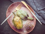Halved fresh artichoke and sprouts on pink ceramic plate on table — Stock Photo