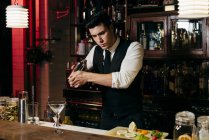 Giovane elegante barman che lavora dietro un bancone del bar mescolando bevande in uno shaker — Foto stock