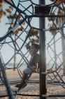 Cheerful African American boy laughing and looking away while sitting on net on playground on beach — Stock Photo