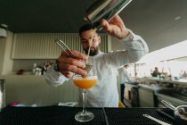 Bartender pouring cocktail from shaker in glass in bar — Stock Photo
