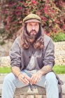 Стильный бородатый мужчина с длинными волосами сидит в парке и думает: — стоковое фото
