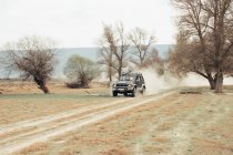 Позашляховик їде по пиловій дорозі поблизу безлистяних дерев під час подорожі по сільській місцевості — стокове фото