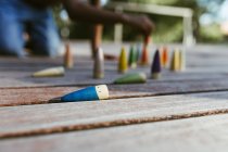 Irreconocible niño afroamericano sin camisa sentado en la superficie de madera y jugando con conos de colores en el día soleado - foto de stock