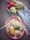 Alcachofras frescas inteiras e cortadas pela metade colocadas na placa cerâmica rosa na mesa — Fotografia de Stock