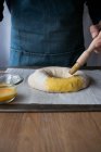 Unrecognizable male cook brushing to covering fresh dough with egg yolk while preparing Rosca de Reyes in kitchen. — Stock Photo