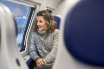Молода весела жінка дивиться через вікно в поїзді, сидячи — стокове фото