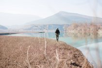 Вид ззаду чоловіка з рюкзаком, що стоїть на березі озера та рибалить у сонячний день у природі — стокове фото