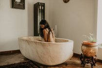 Vista lateral de una mujer bonita tomando un baño en una casa rústica - foto de stock
