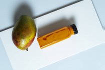 Frullato vegano al mango e zucca in bottiglia su lavagna bianca con frutta — Foto stock